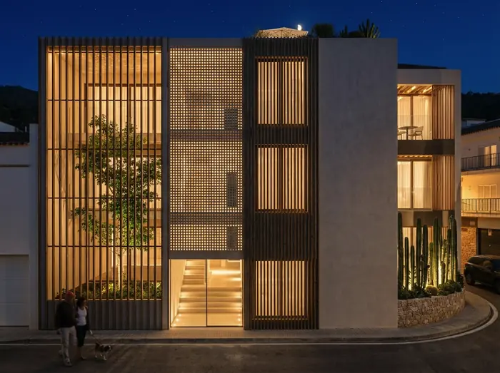 Façana de Tamariu Residences de nit, amb les gelosies de fusta il·luminades des de l'interior